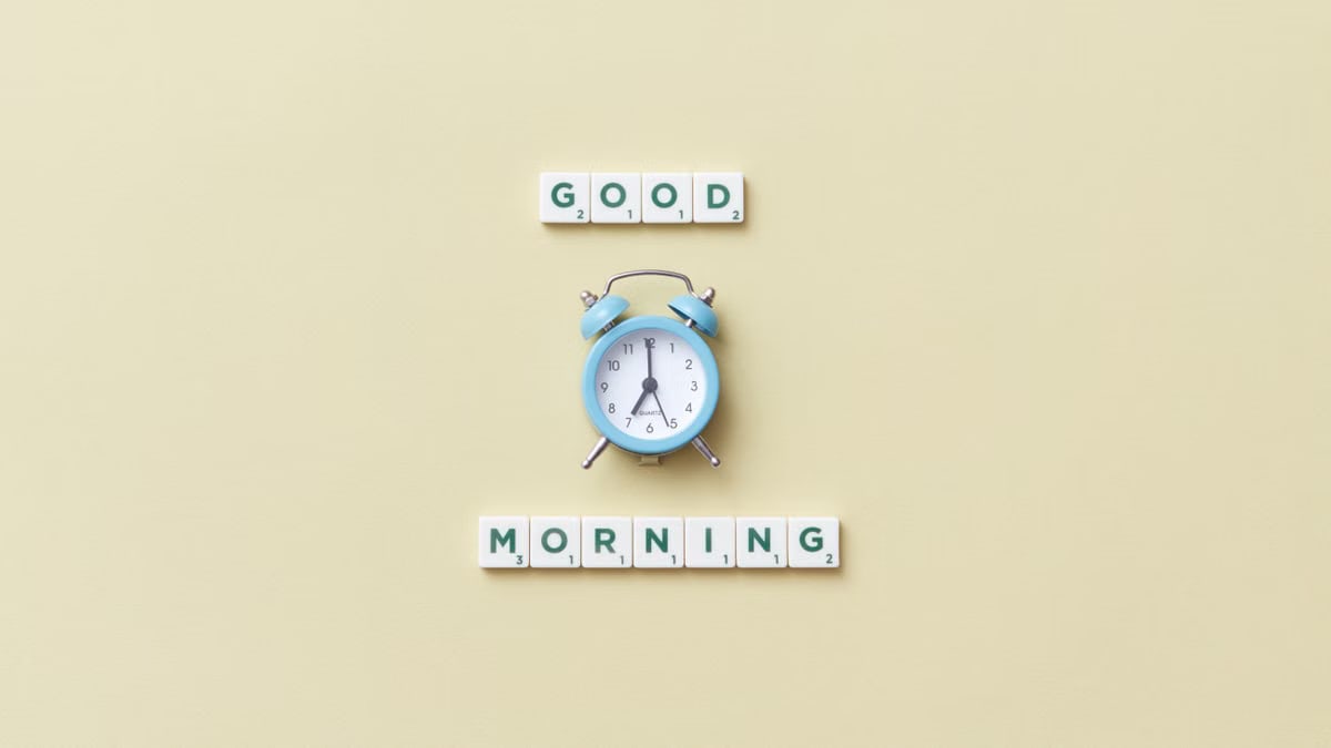 Blue alarm clock with 'Good Morning' scrabble tiles on yellow background.